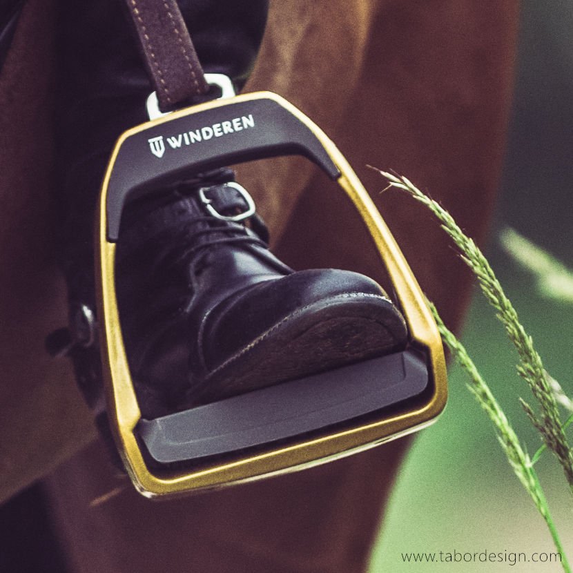 Żółte strzemię jeździeckie zawieszone na brązowym puślisku. W strzemieniu czarny but z klamrą.