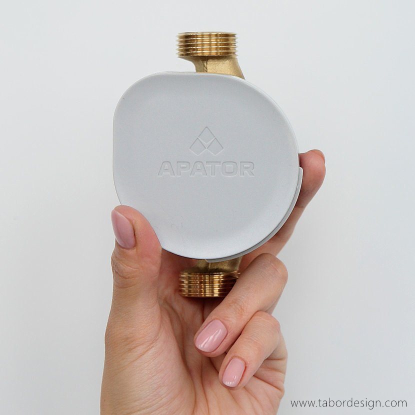 Wodomierz Apator trzymany w kobiecej dłoni. Tarcza liczydła zasłonięta klapką z logo firmy. Kształt klapki to kropla wody.